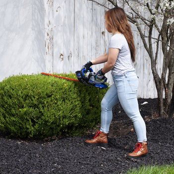 Woman trimming hedge with Westinghouse hedge trimmer against a white fence