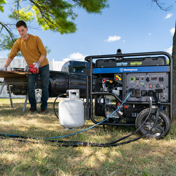 Westinghouse | WGen12000DF portable generator connected to a propane tank sitting on the grass. A man is working in the background.