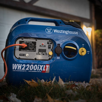 Westinghouse | WH2200iXLT inverter generator on the ground in front of a house. It is dark but the house lights are on.